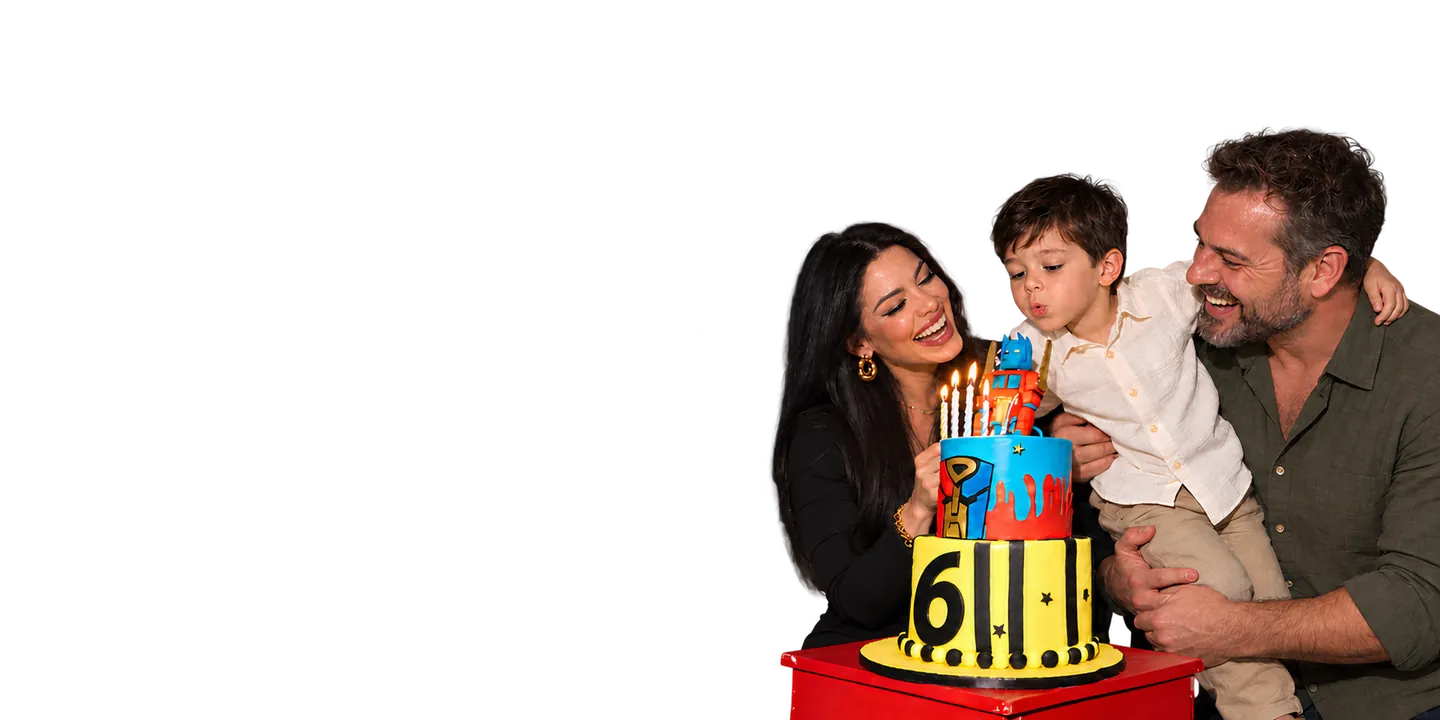 A child blowing out birthday candles with his parents beside a giant yellow robot at a themed party.